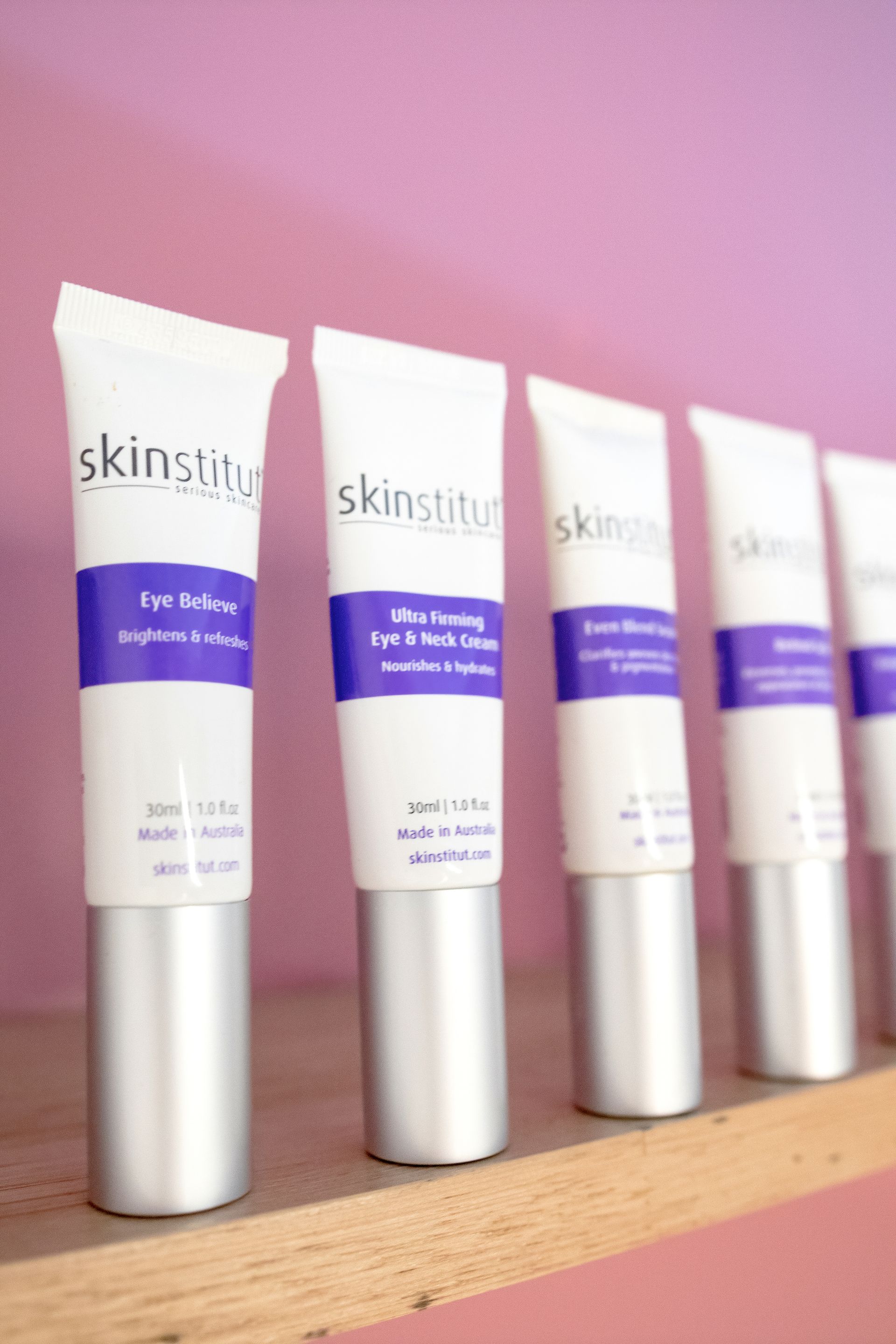 White skincare tubes with purple accents lined up on a shelf, against a pink wall.  — Admire Skincare and Beauty in Taree, NSW