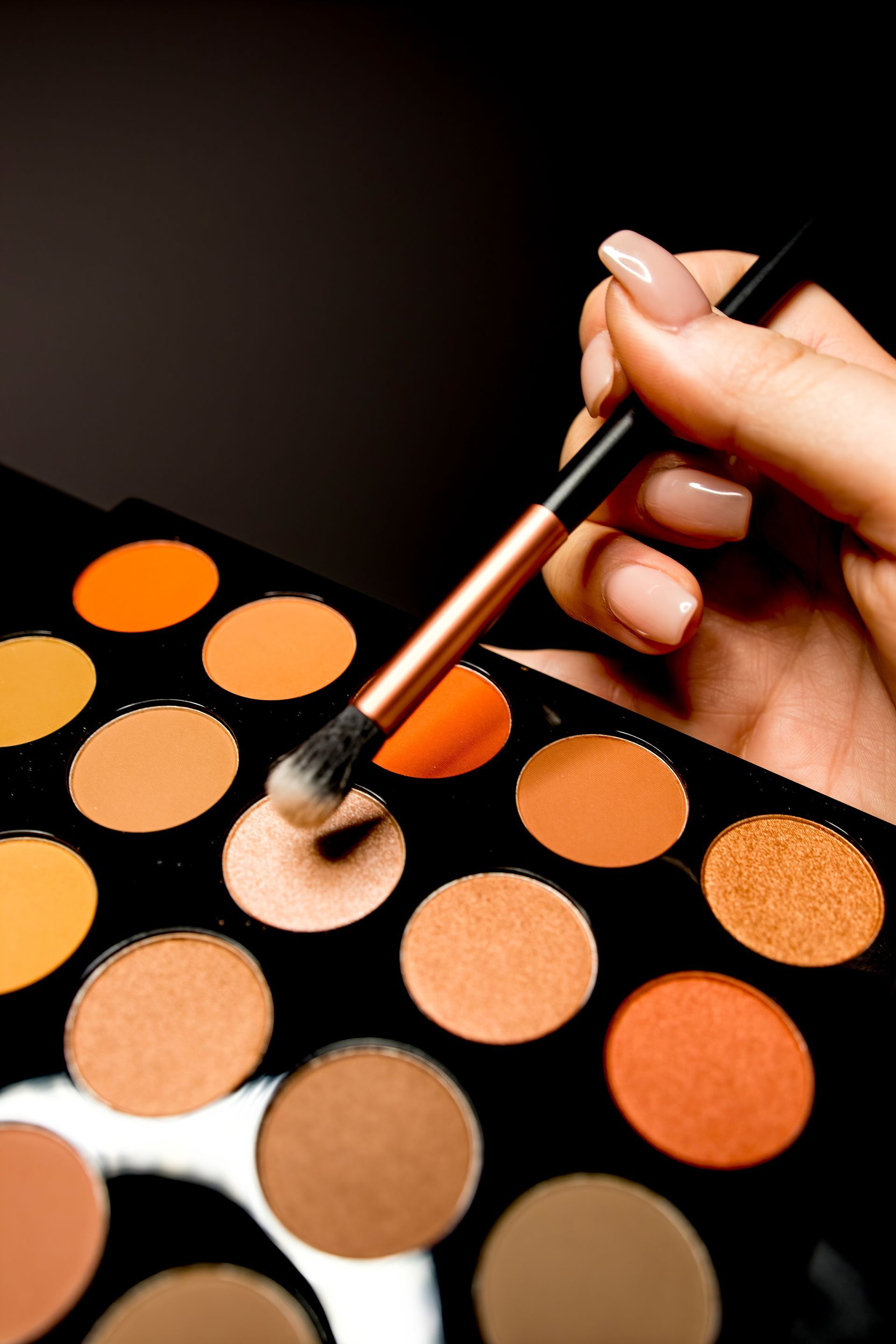 Hand holding a makeup brush over an eyeshadow palette with warm-toned shades. — Admire Skincare and Beauty in Taree, NSW