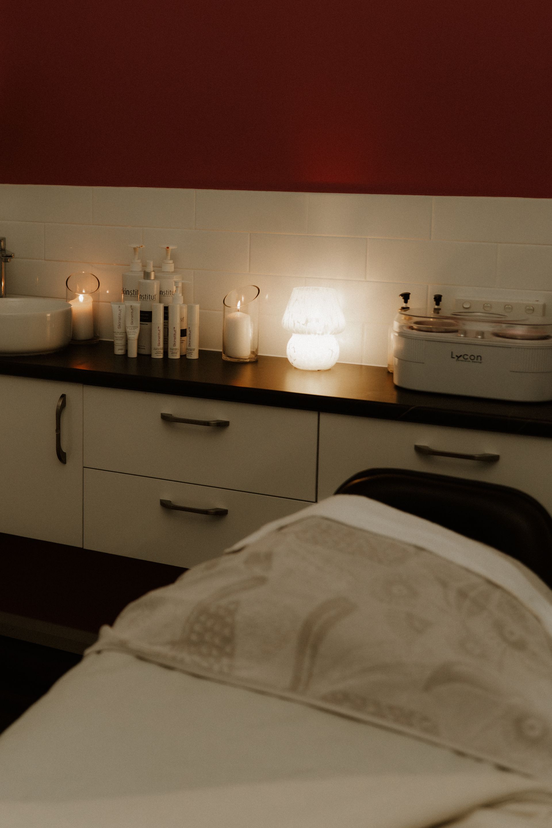 Spa treatment room with candles, products, and a massage bed covered with a white sheet.