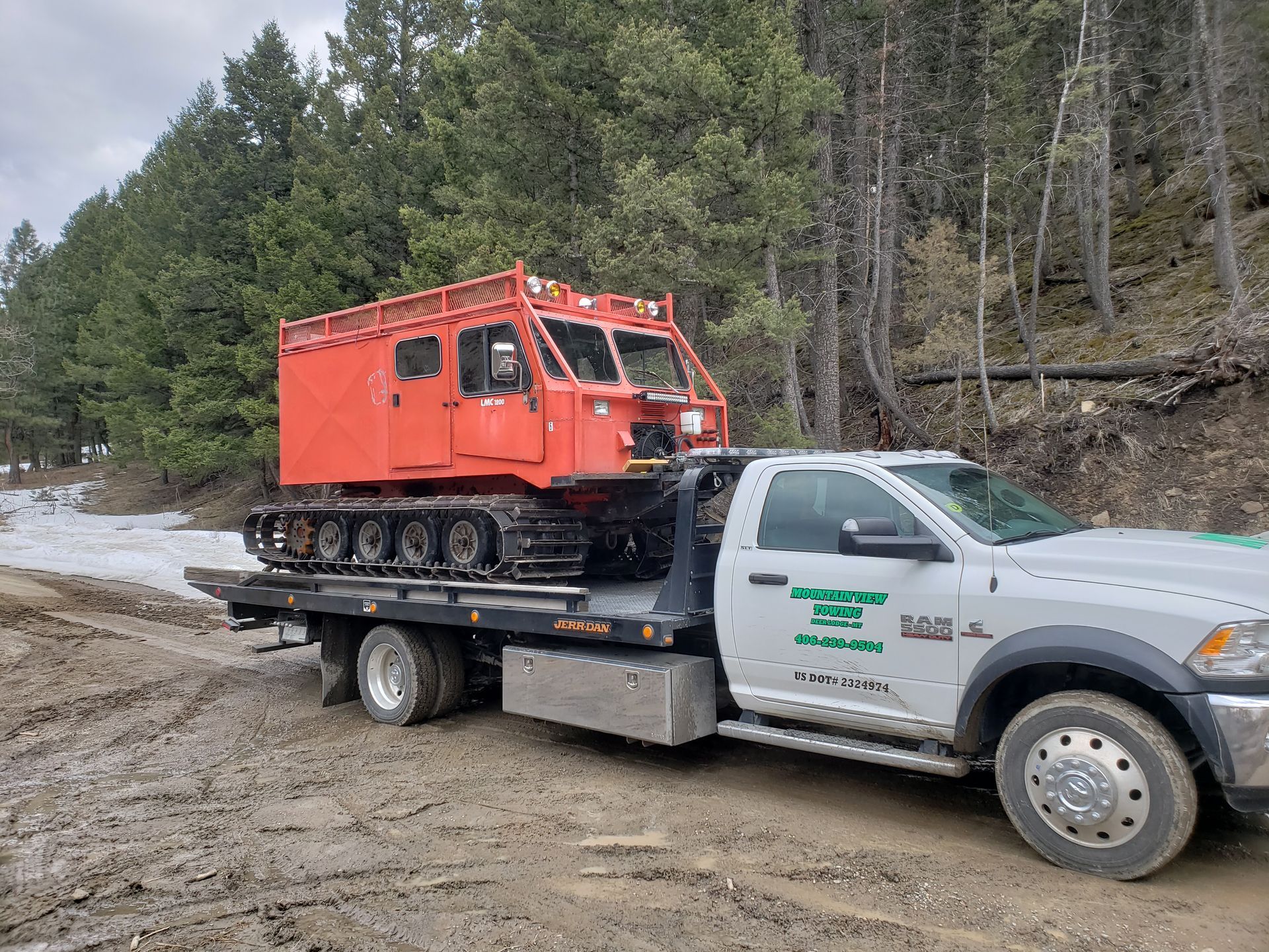 A gray car loaded on a flatbed tow truck outdoors on a sunny day.
