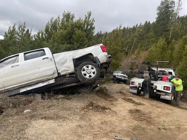 A roadside assistance worker kneels to secure a chain to a car wheel, a tow truck behind.