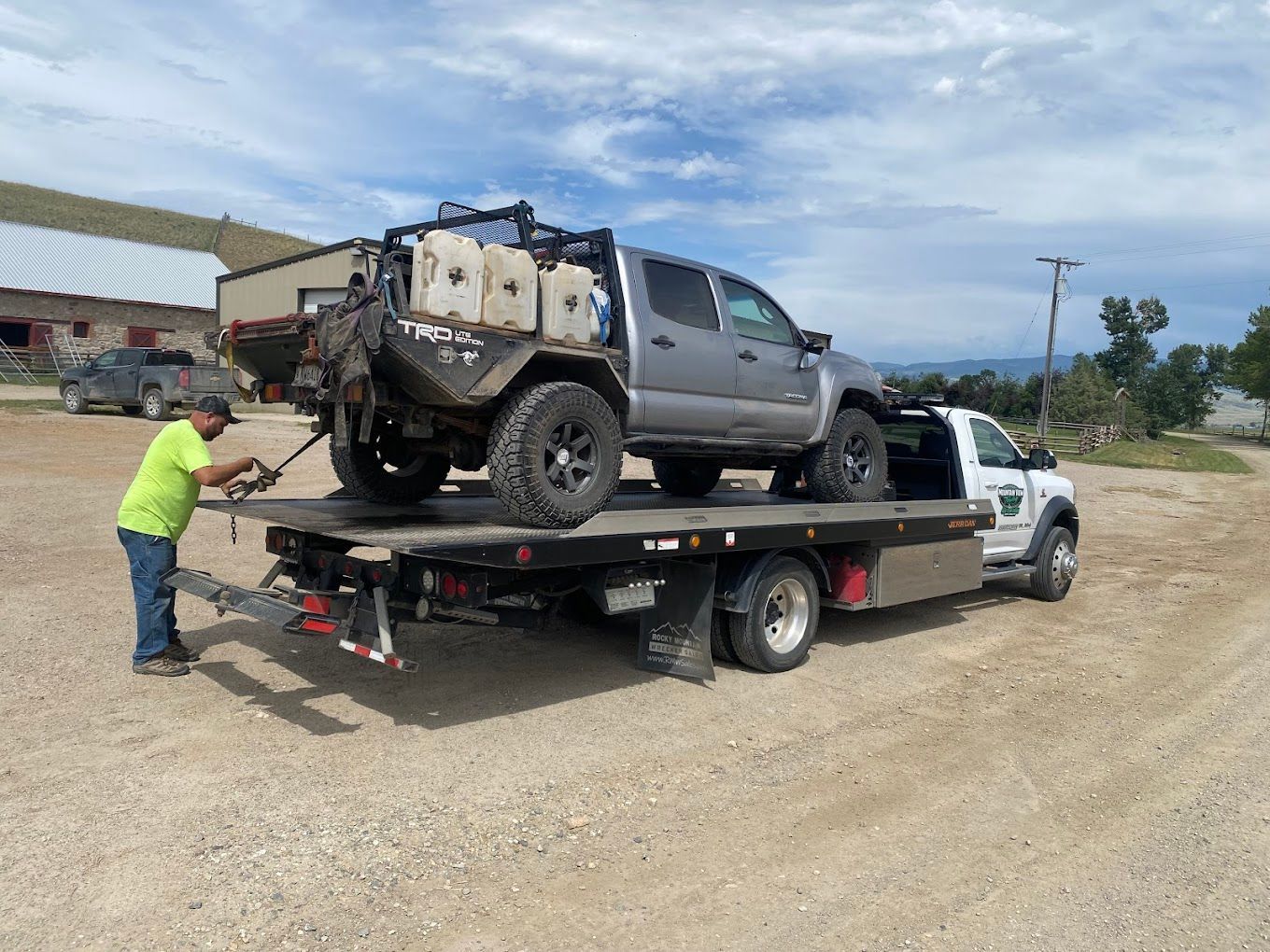 A gray car loaded on a flatbed tow truck outdoors on a sunny day.