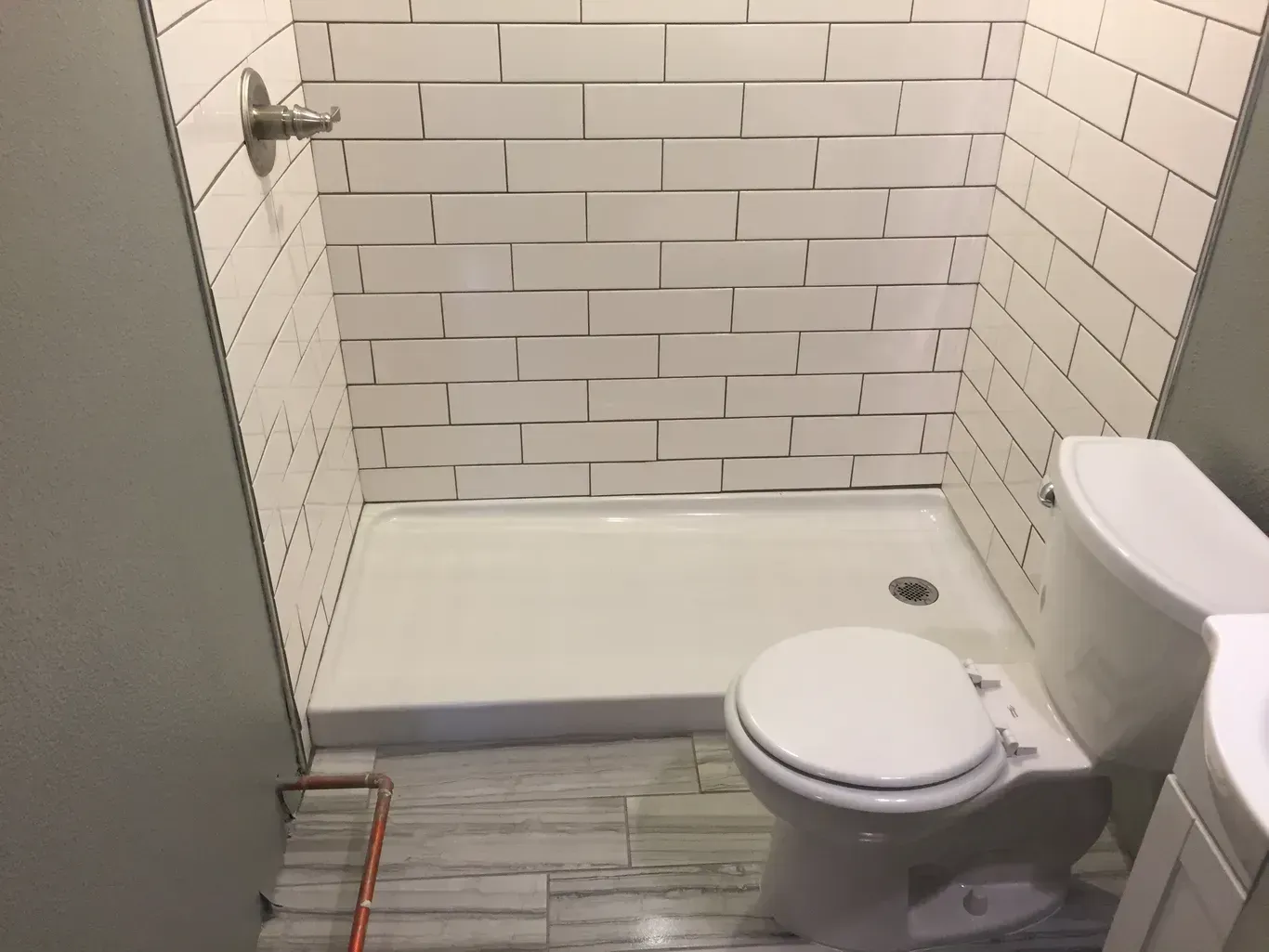 A small bathroom with a white tiled shower, toilet, and gray walls.