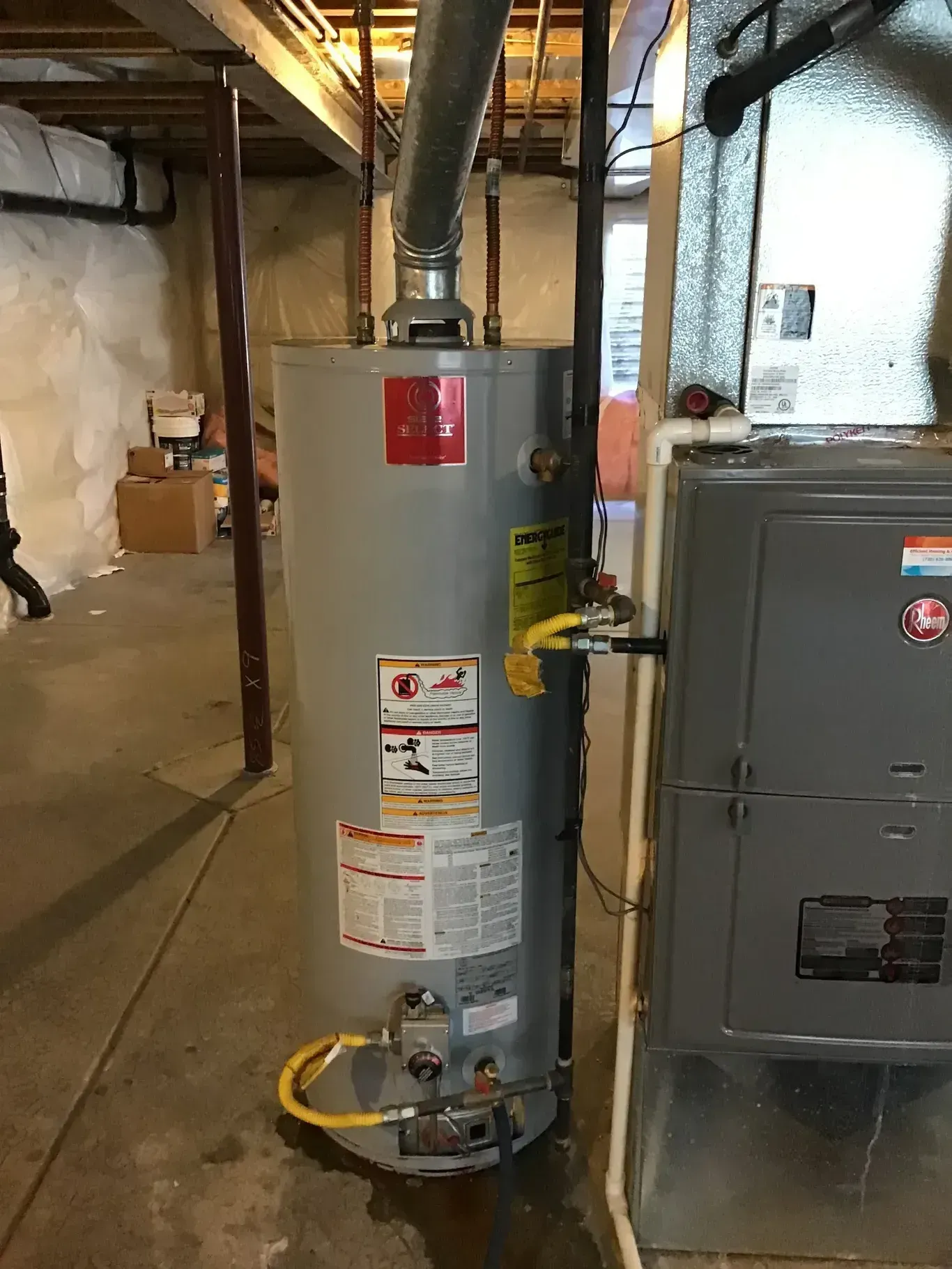 A tall gray water heater and a furnace unit in a basement setting.