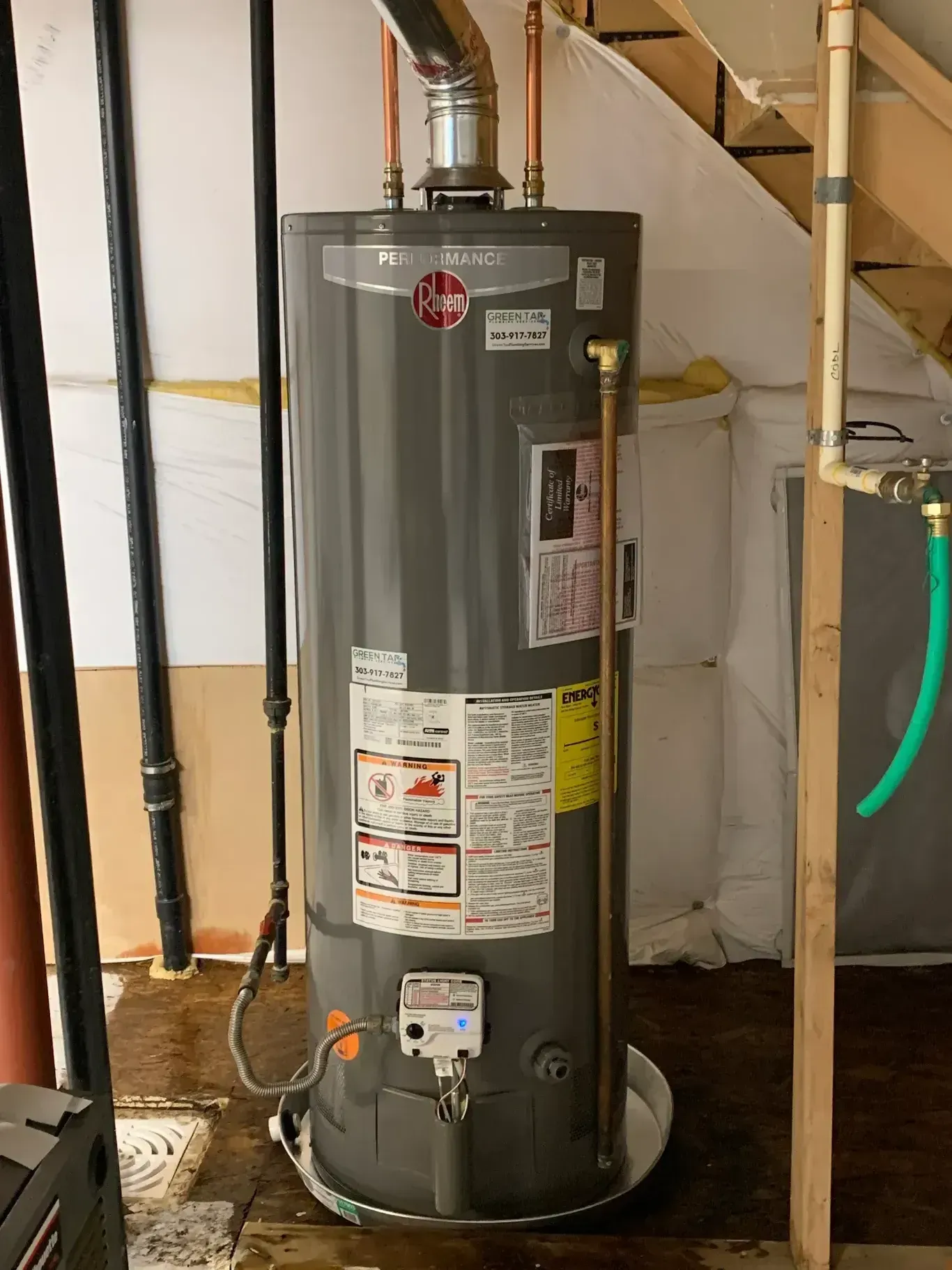 Gray water heater in a basement, with copper pipes and a vent.