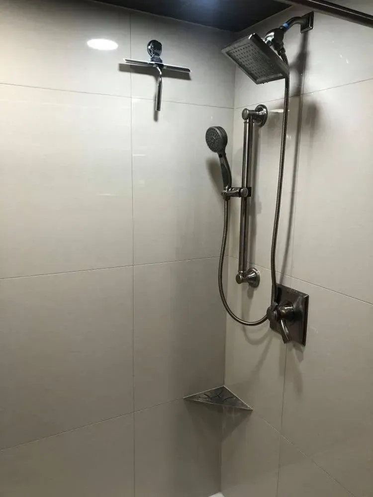 Modern shower with multiple showerheads, a handheld wand, and built-in shelf; light gray tile walls.