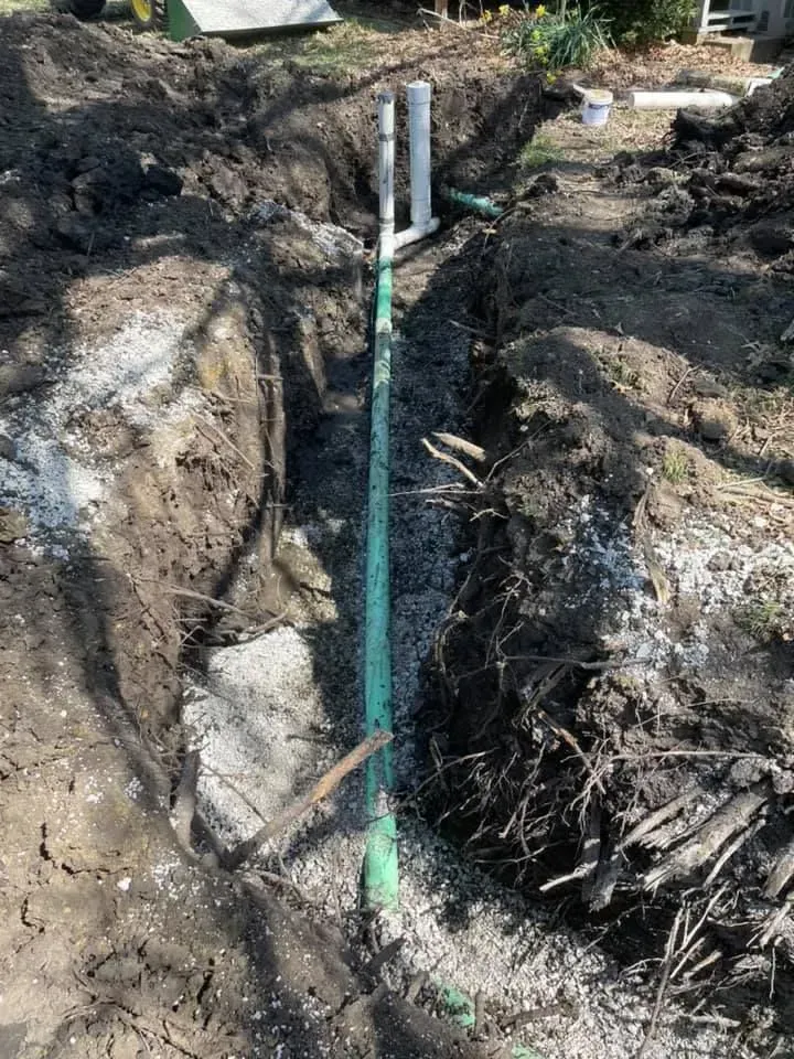 A trench with green pipes, gray gravel, and white PVC pipes in a yard.