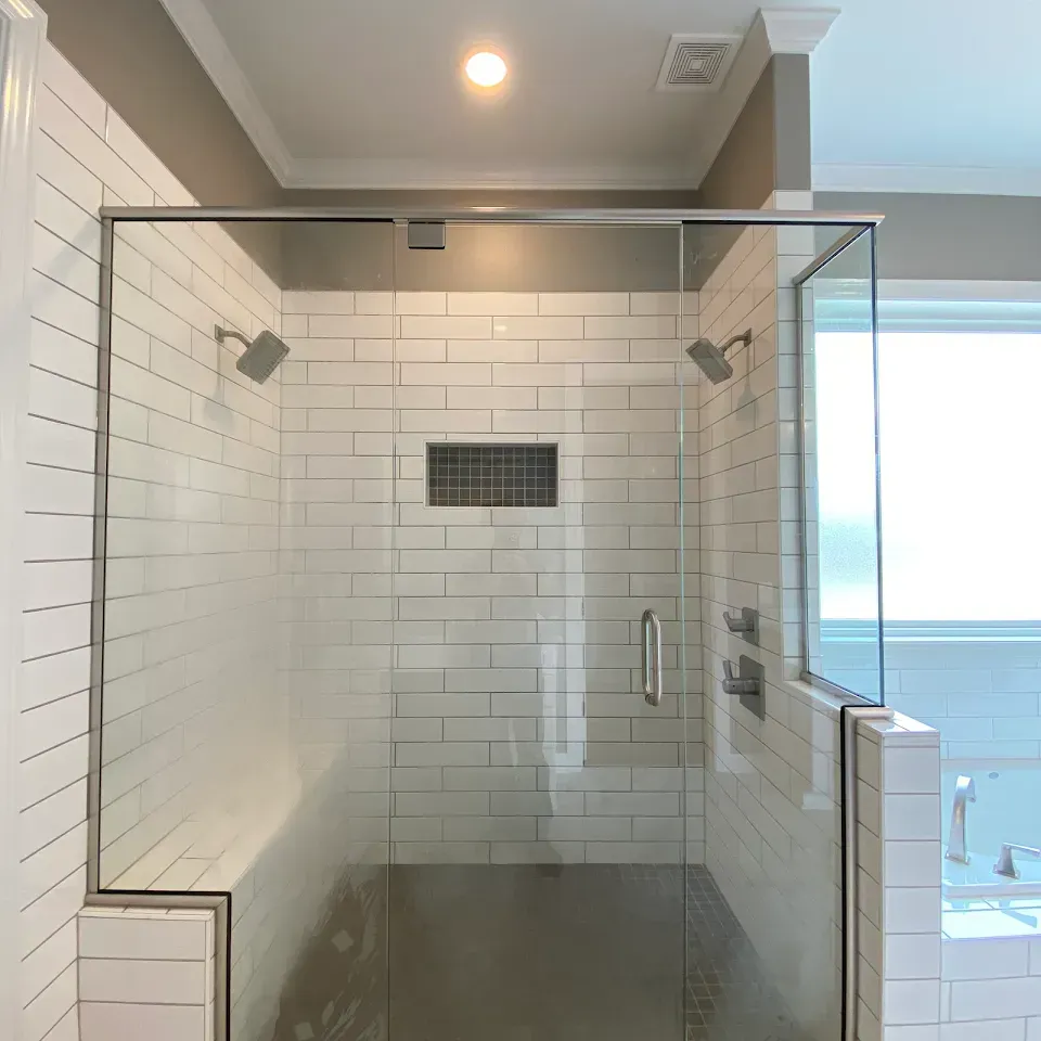 Glass-enclosed shower with white subway tiles, a recessed shelf, and two shower heads.