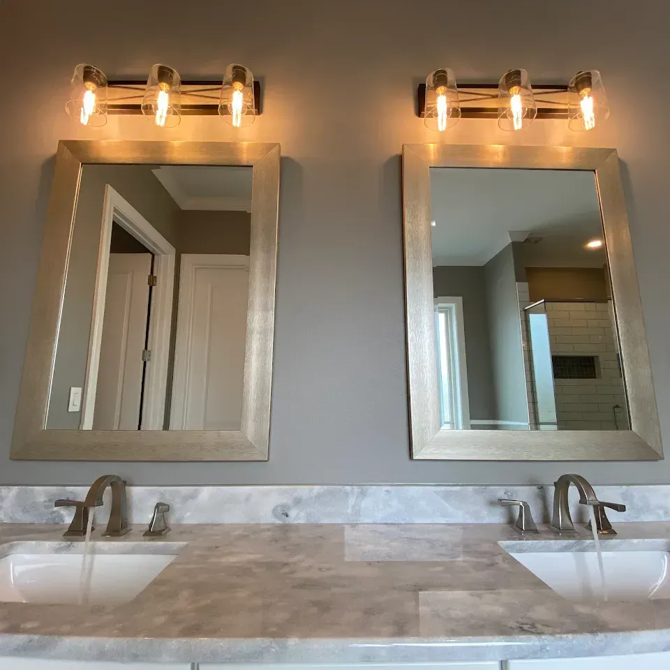 Two mirrors above sinks in a bathroom with silver frames and light fixtures.