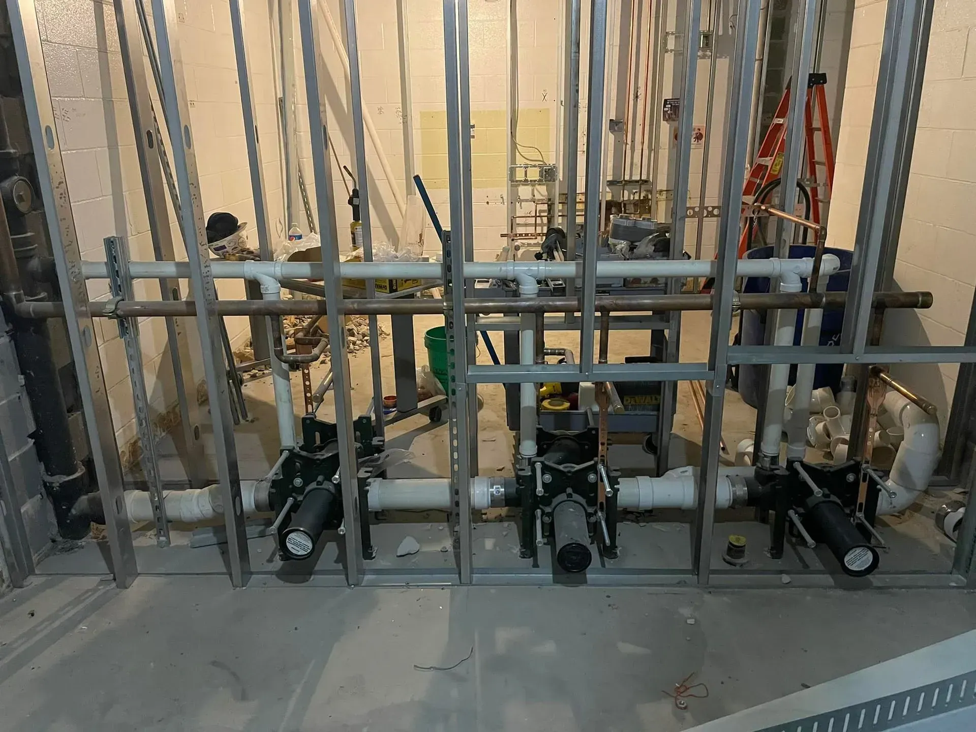 Plumbing pipes and valves within a metal stud framework. The setting appears to be an unfinished construction area.