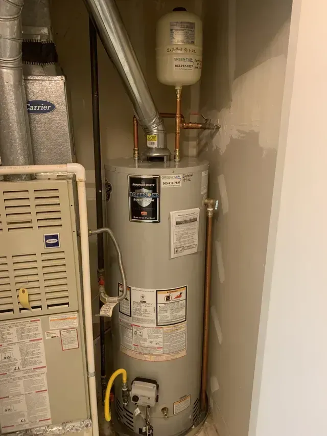 A water heater and furnace unit in a utility closet with a white wall.