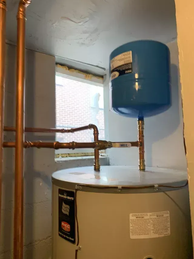 A water heater with a blue expansion tank and copper pipes in a basement.