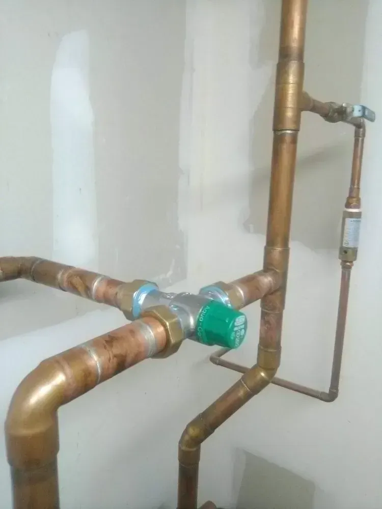 Copper pipes and valves, including a green handled valve, are installed on a light beige wall.