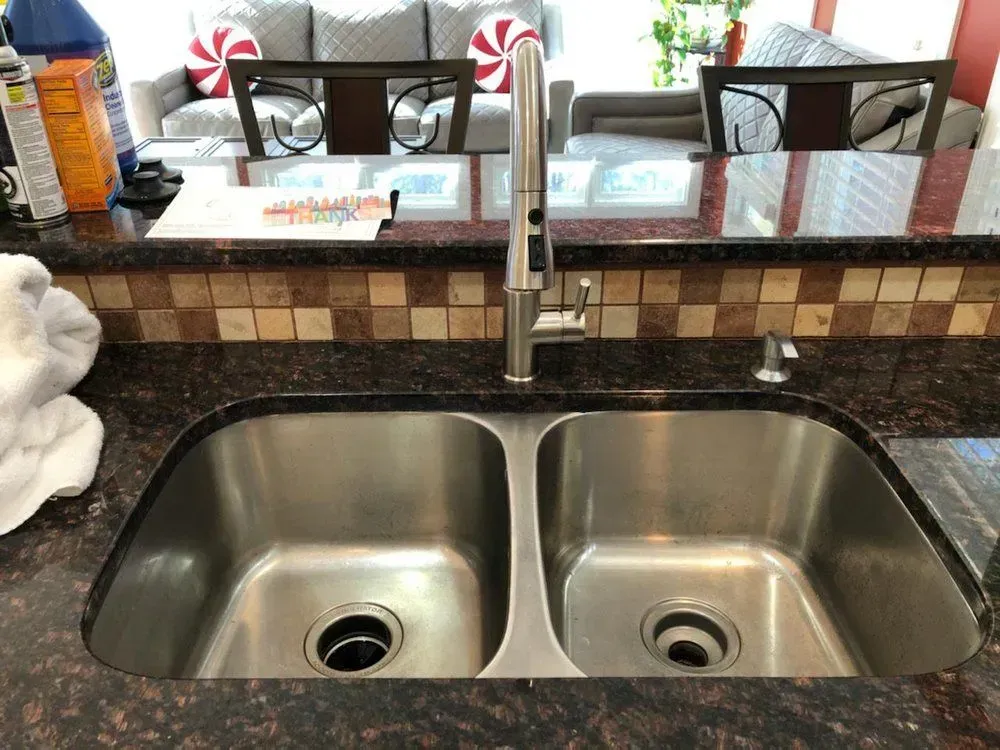 Stainless steel double kitchen sink with faucet, granite countertop, and tiled backsplash.