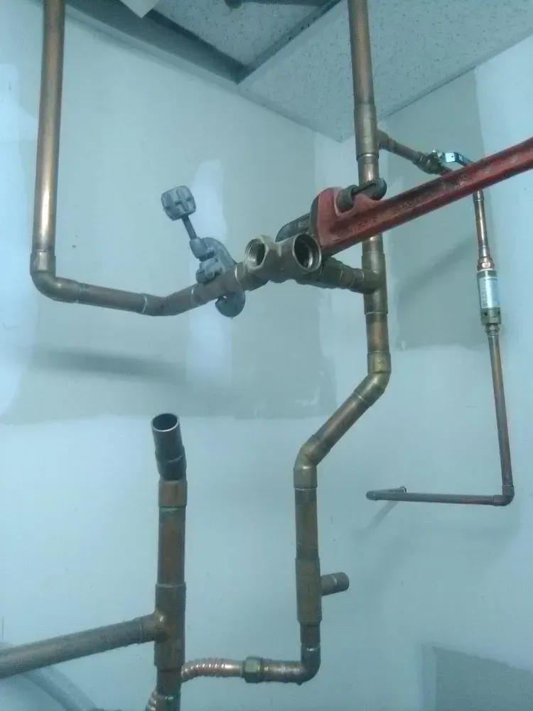Copper pipes and fittings being worked on with a wrench in a utility room.