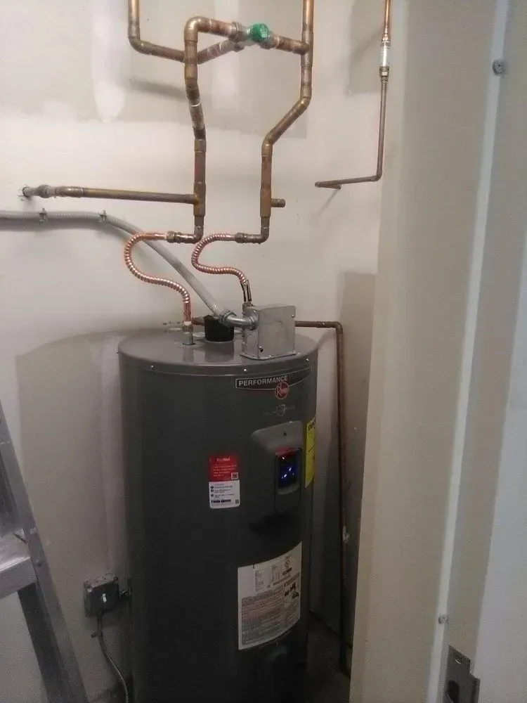 Copper pipes connected to a gray water heater against a white wall.