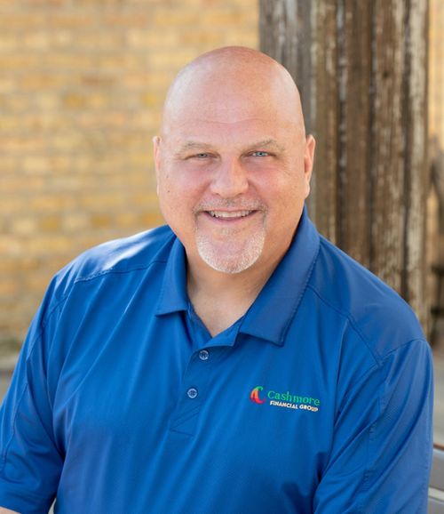 A bald man with a beard is wearing a blue shirt and smiling.