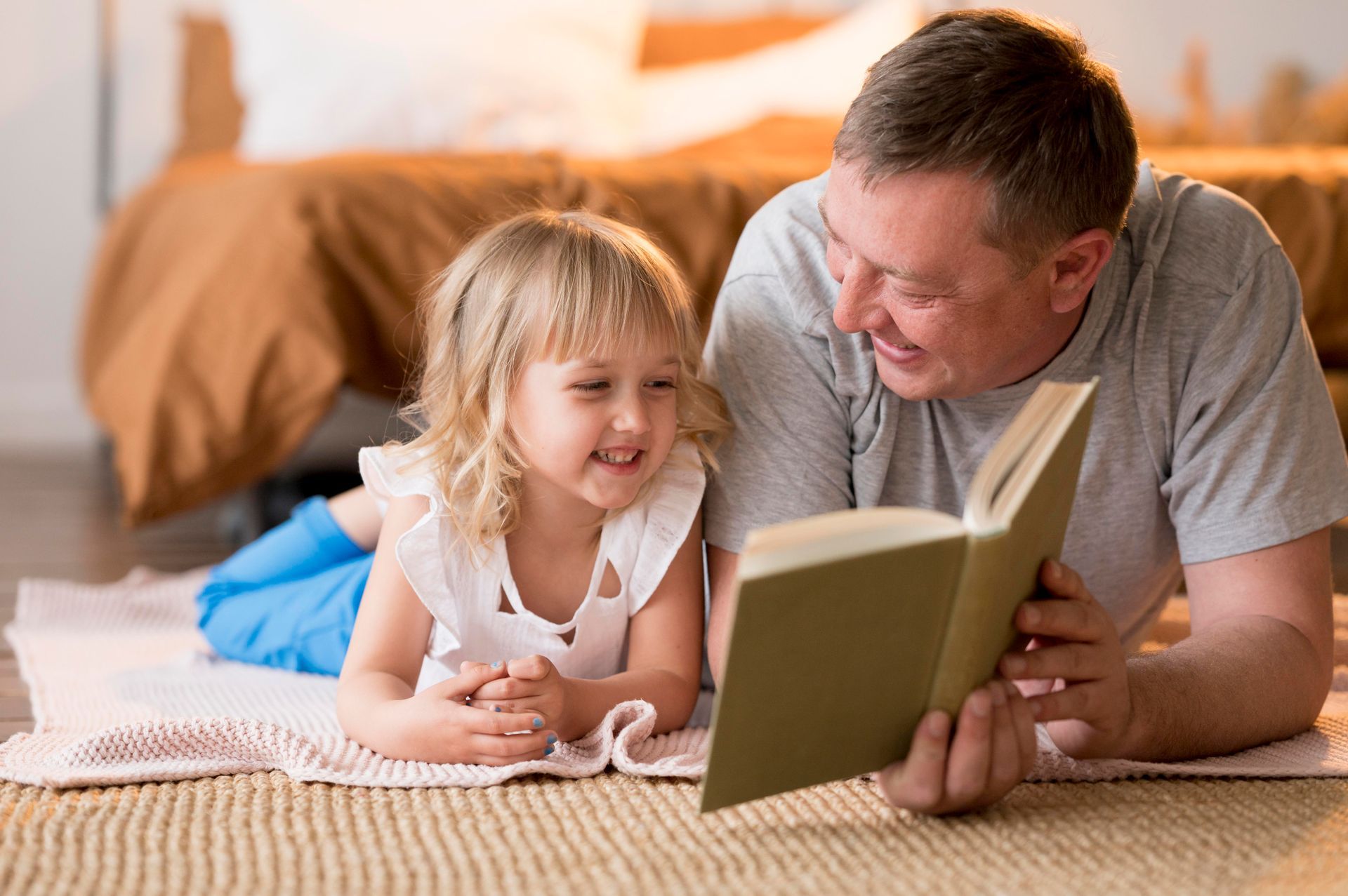 A man and a little girl are laying on the floor reading a book together.