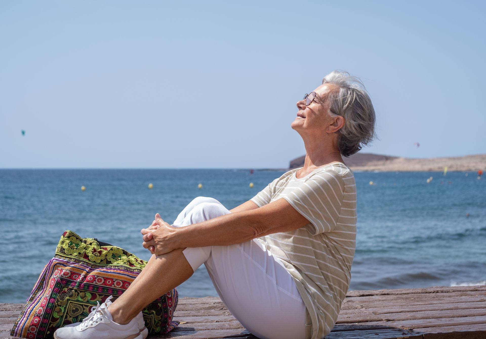 An elderly woman is sitting on a dock near the ocean.