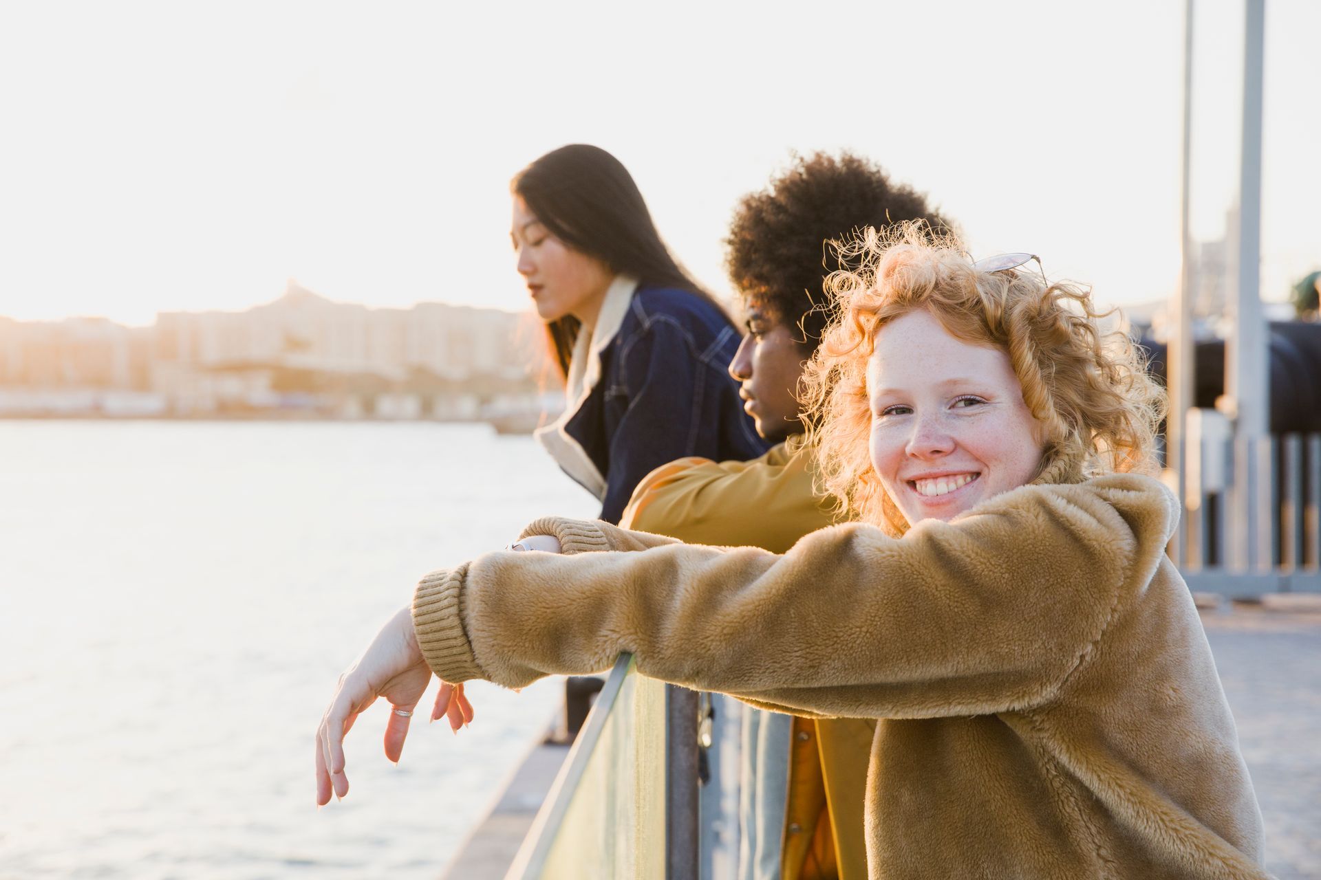 A group of young women are leaning on a railing overlooking a body of water.