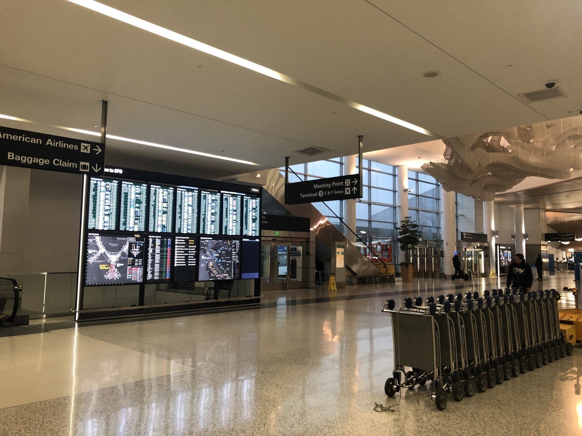 A line of luggage carts at the right within the hallway of an airport terminal at SFO. On the left, walls of wayfinding signage are seen.