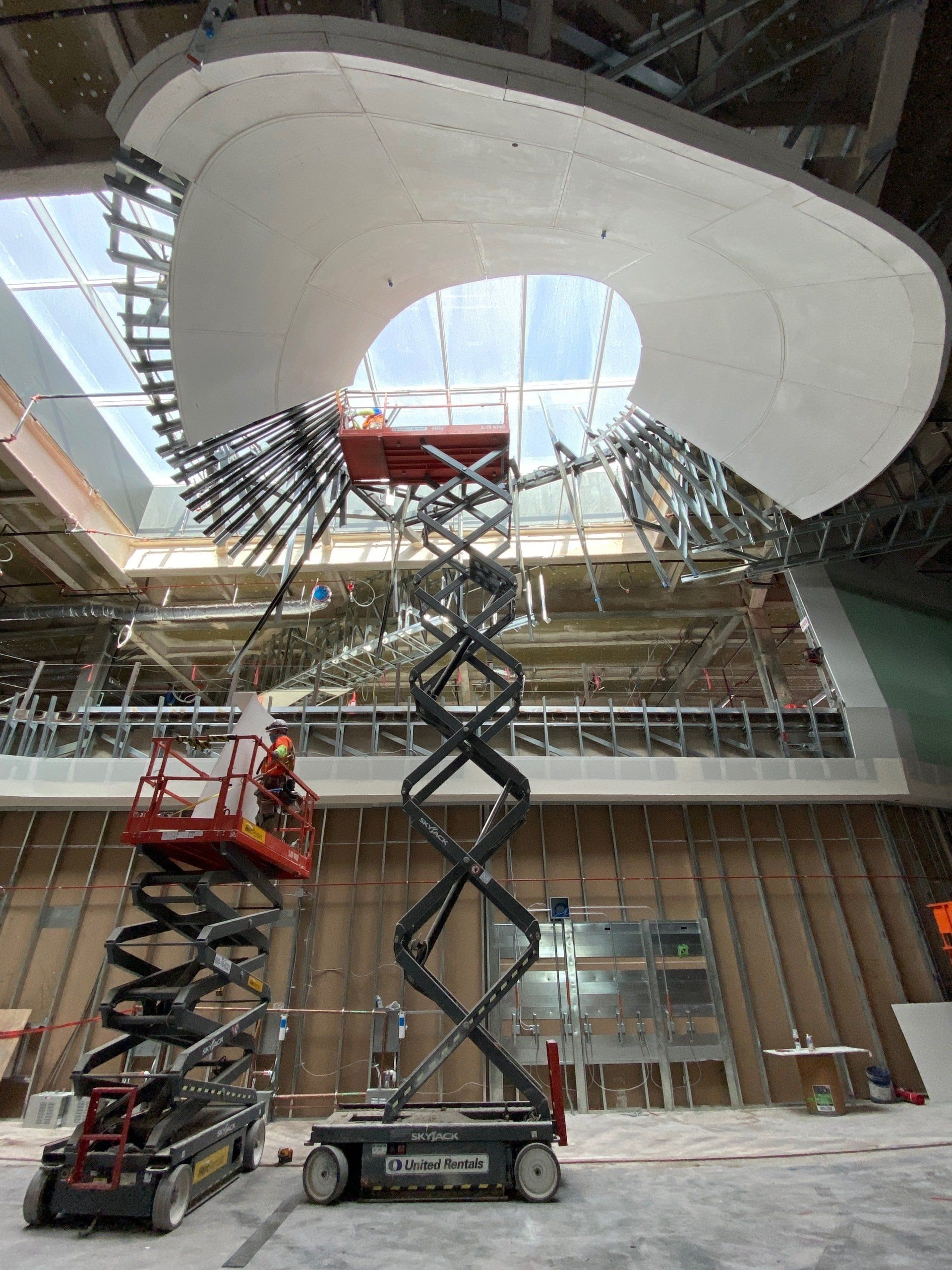 The inside of Harvey Milk Terminal at SFO, with cranes stretching up towards the ceiling during construction of a decorative ceiling element.