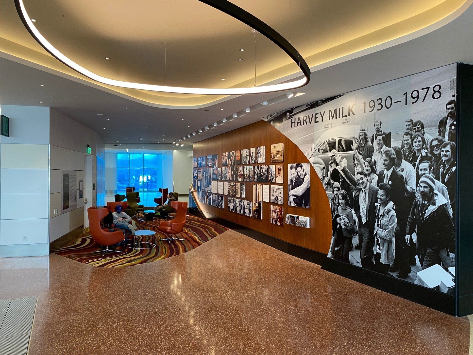 A seating area within the Harvey Milk terminal, showing orange plush chairs around a table on the left, and walls decorated with vinyl graphics on the right.