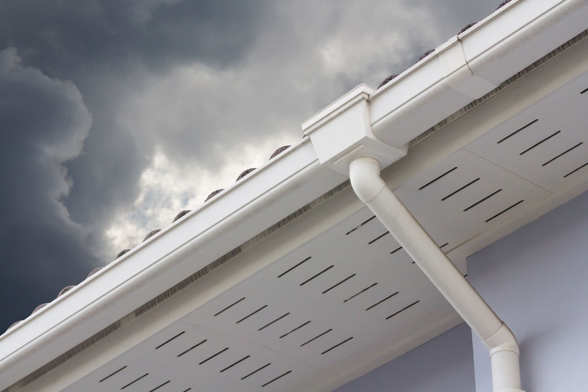 White house eaves and gutter against a dark cloudy sky