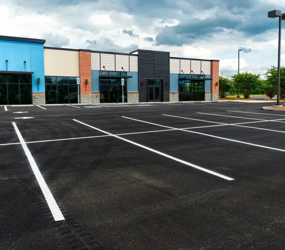 Empty parking lot in front of a blue-and-black commercial building under cloudy skies