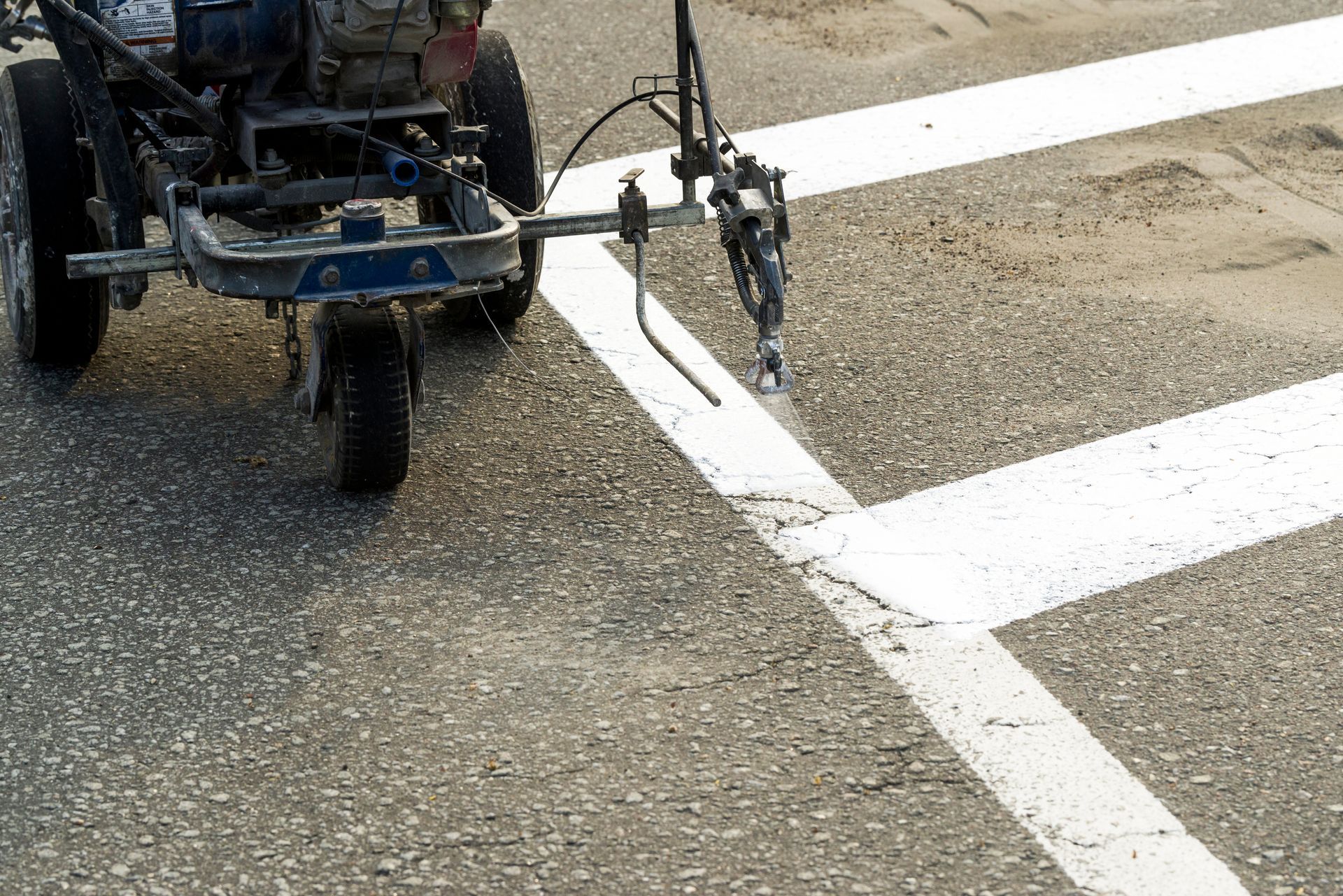 A line-striping machine sprays white paint onto an asphalt road to mark a crosswalk.