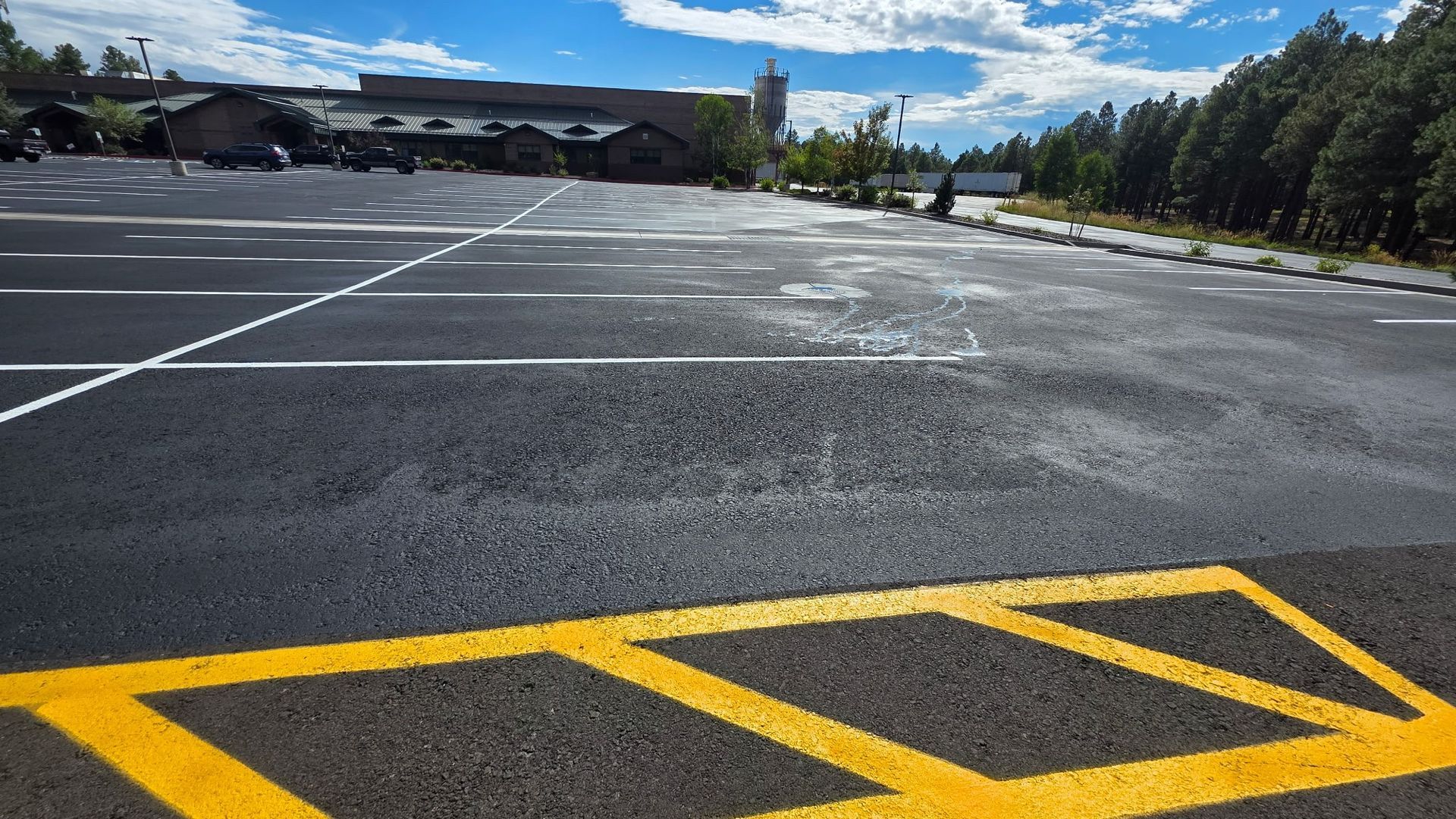 A yellow plate compactor machine levels fresh black asphalt on a road surface.