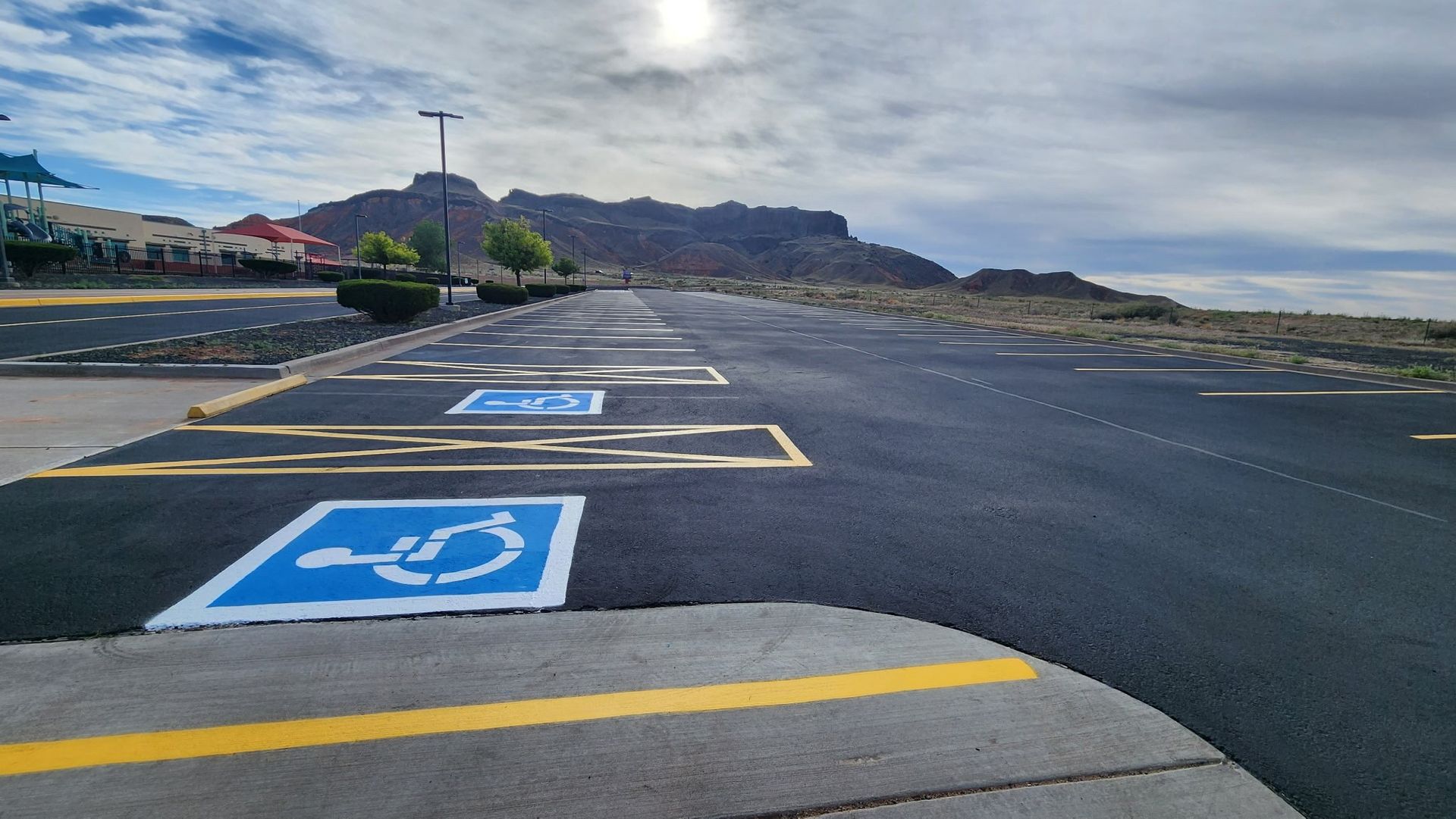 A worker in high-visibility gear uses a long-handled squeegee to spread black sealant over cracks on an asphalt road.