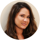 A woman wearing a white shirt and earrings is smiling in front of a window.