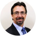 A man wearing a purple shirt and tie is smiling for the camera.