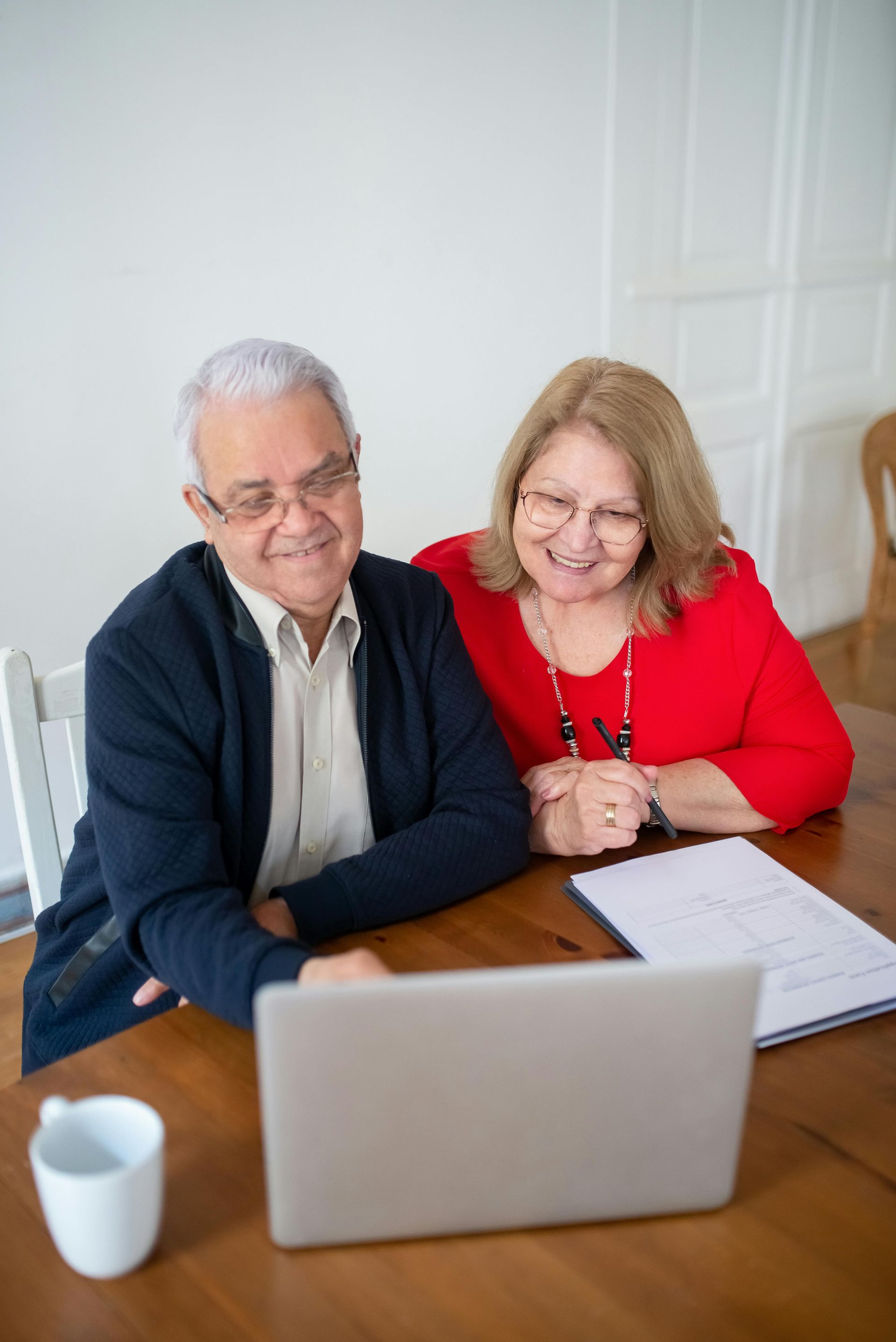 An elderly couple is sitting at a table looking at a laptop computer.