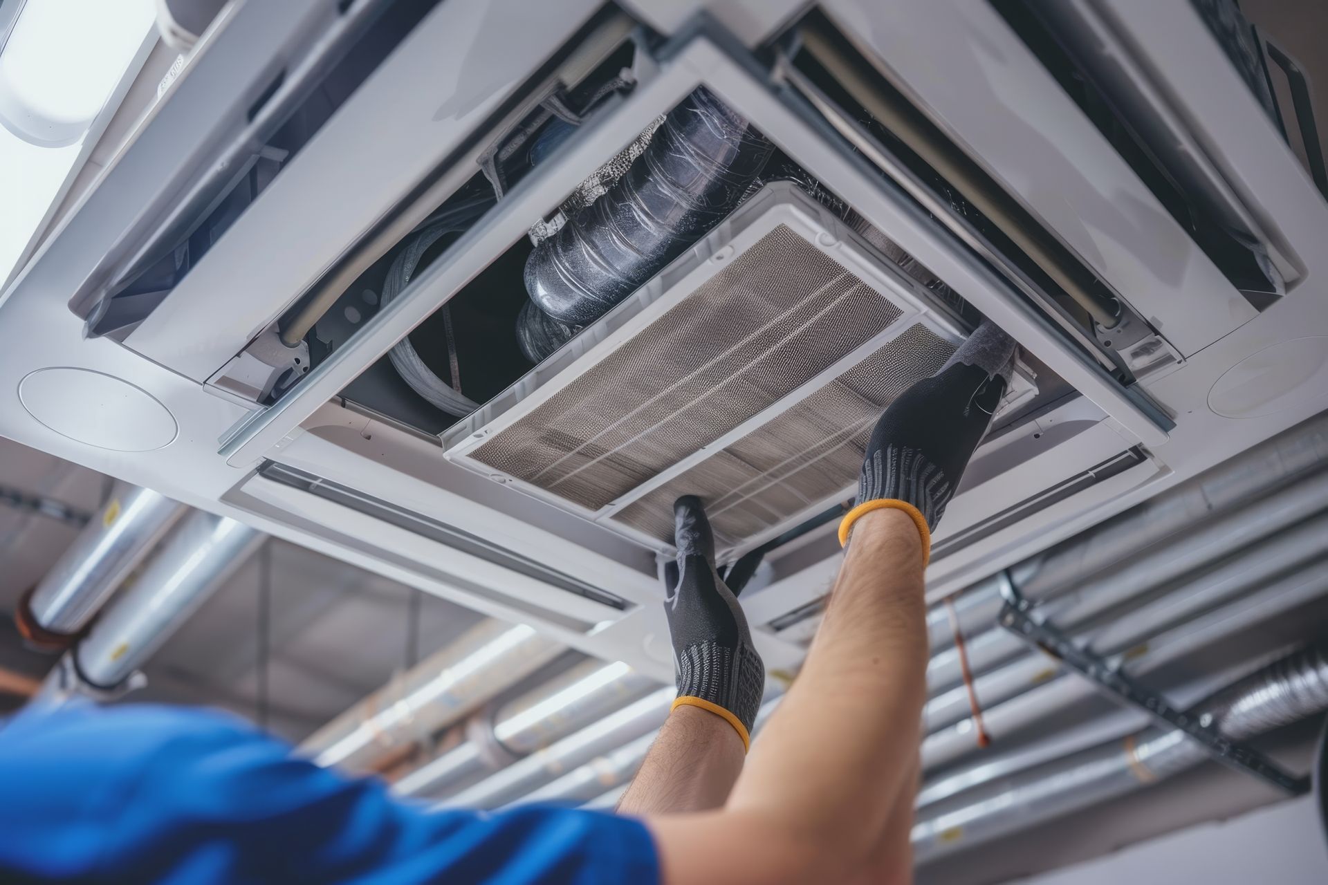 Hands in black gloves removing a ceiling air filter.