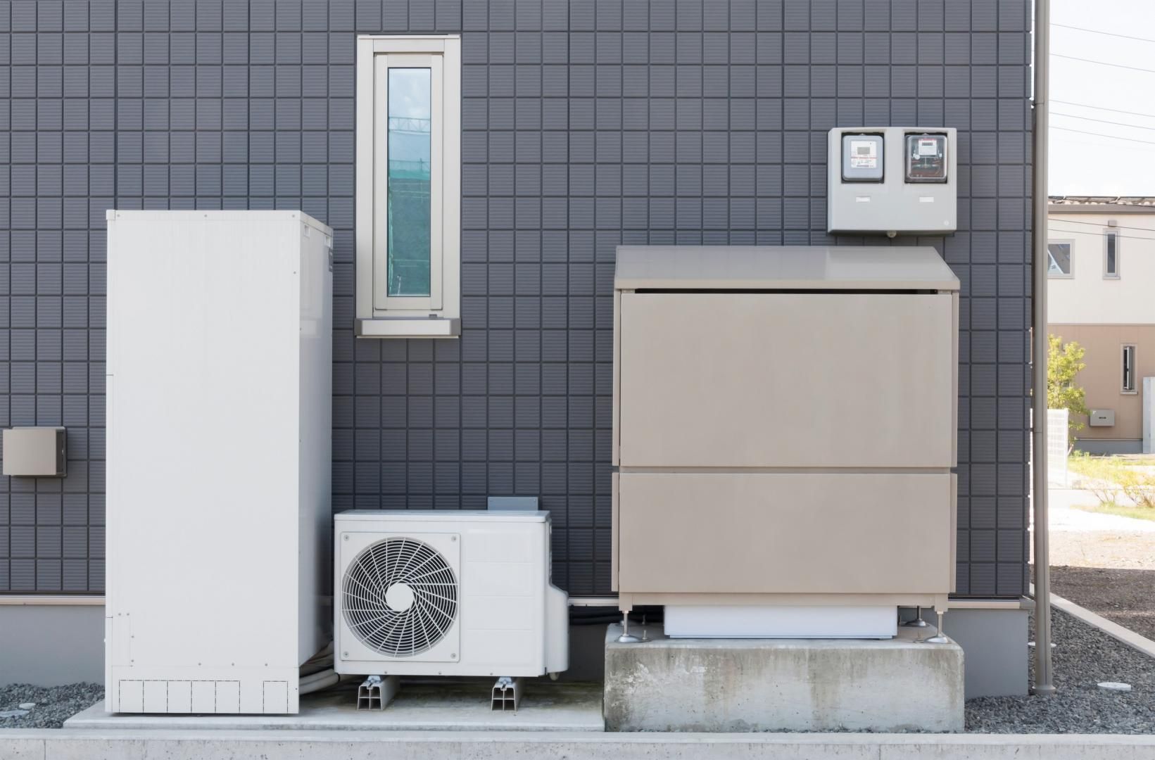 A white air conditioner is sitting on the side of a building next to a window.