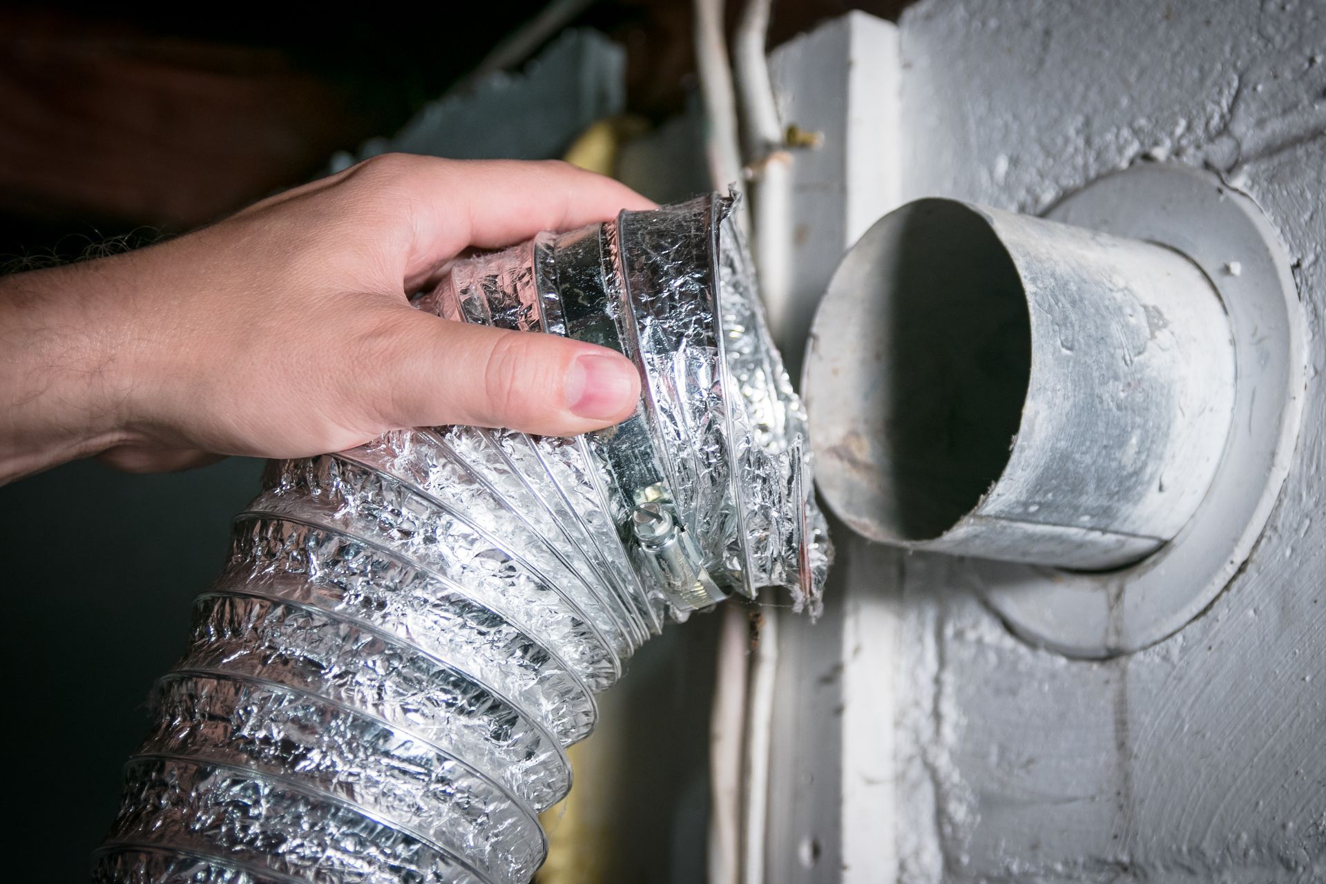 Hand connecting a flexible dryer vent to a metal wall outlet.