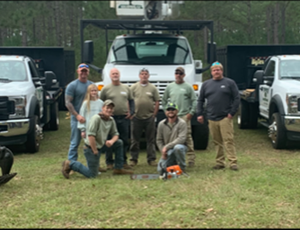 A group of workers with trucks and equipment outdoors. People are posing for a photo.