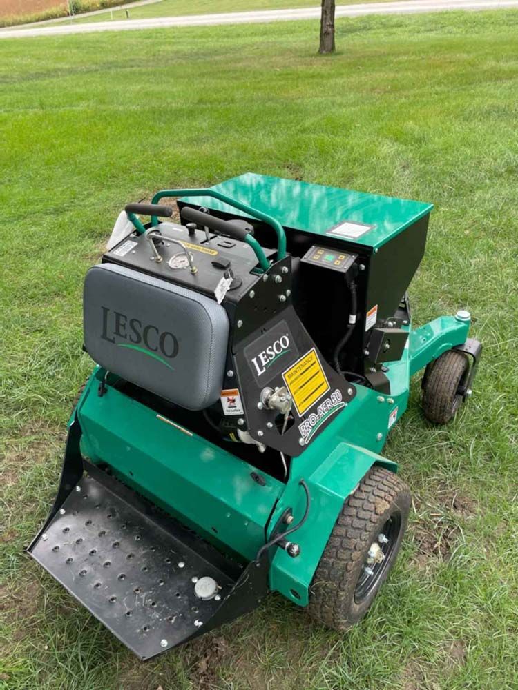 A green lawn mower is sitting on top of a lush green field.