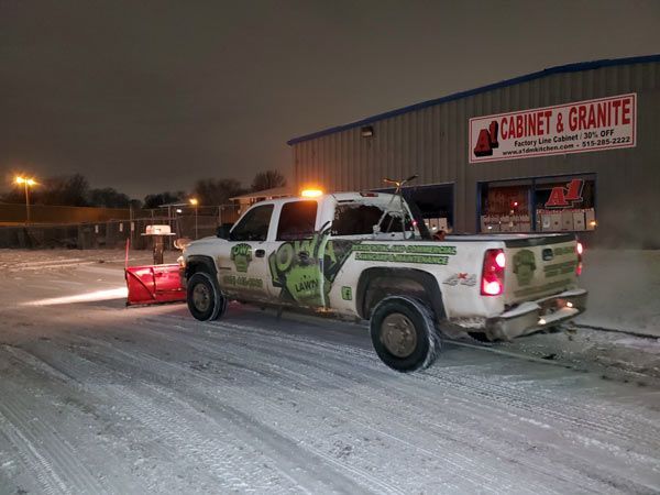 A truck is plowing snow in front of a cabinet and granite store.