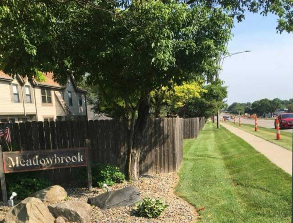 A sign that says meadowbrook is in front of a wooden fence.