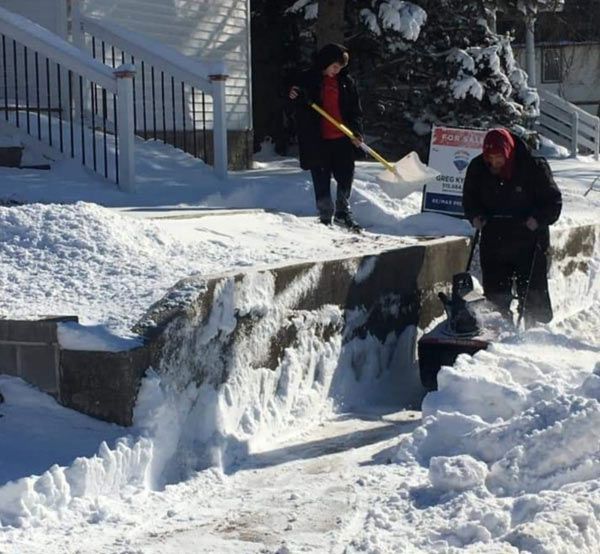 People shoveling snow in front of a house with a sign that says snow removal