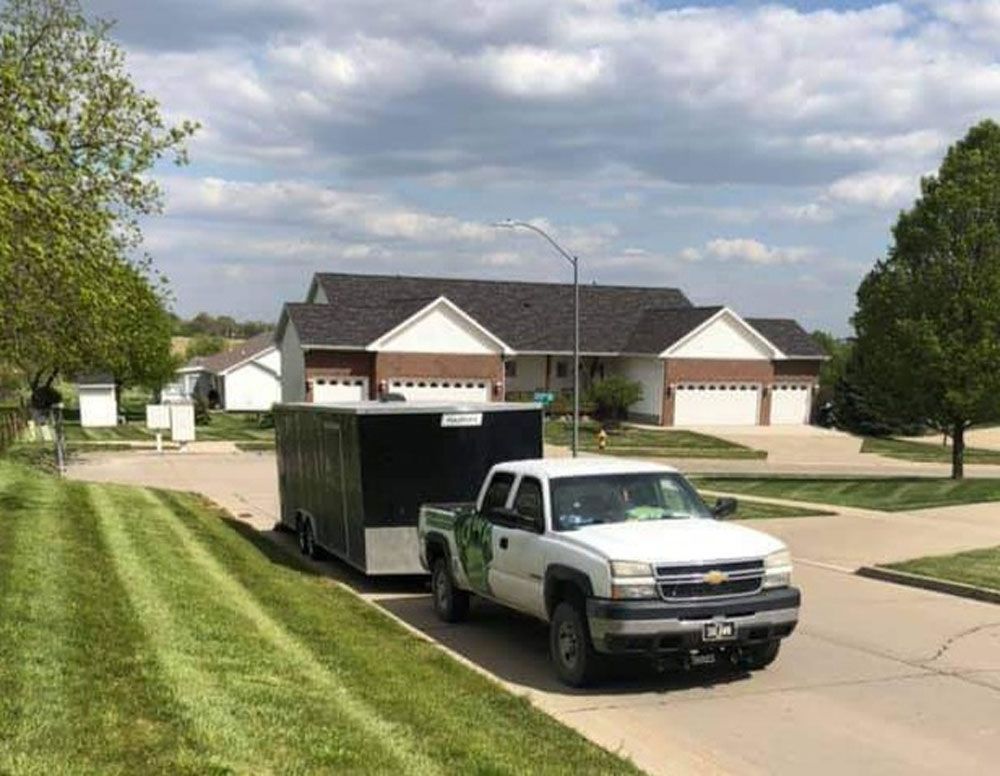 A truck is pulling a trailer down a street in front of a house.