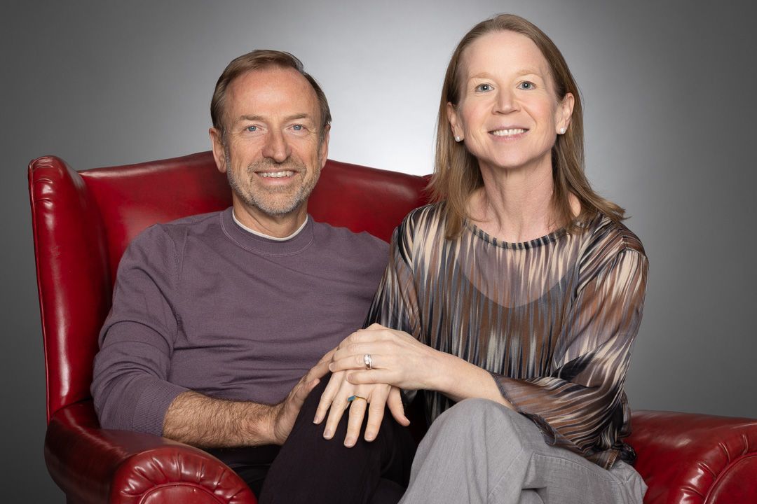 Jerry Michalski and April Rinne are sitting in a red chair holding hands.