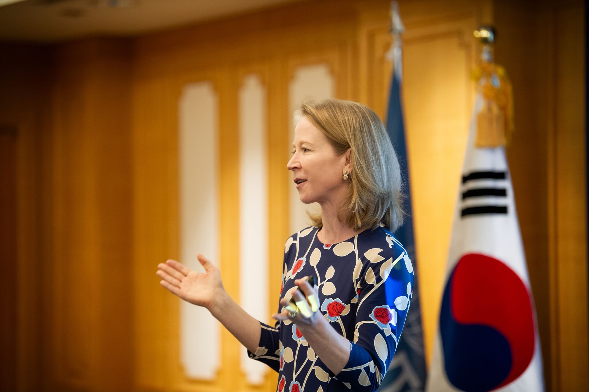 April Rinne is standing in front of two flags and giving a speech.
