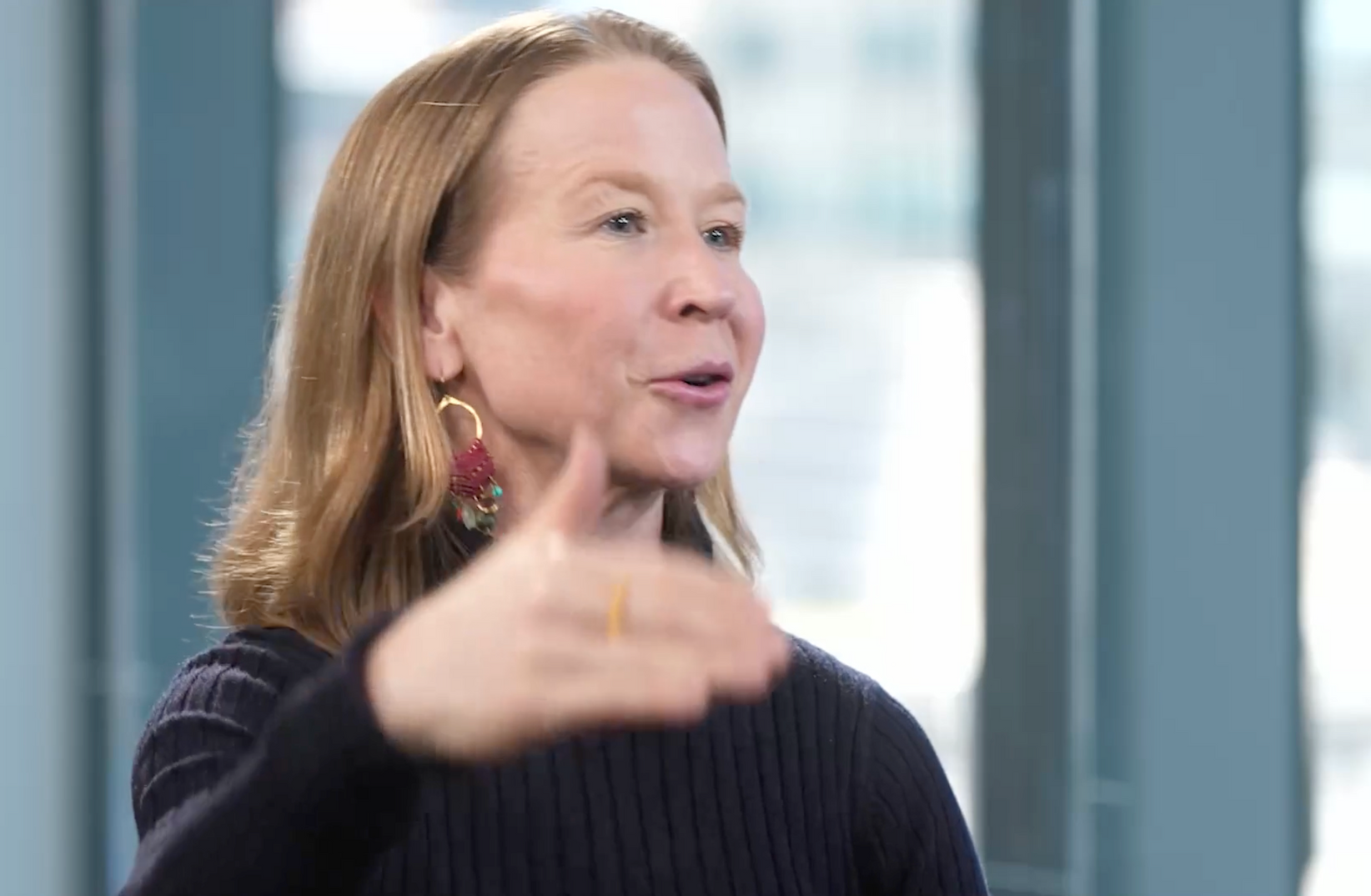 April Rinne is giving a thumbs up sign in front of a window.