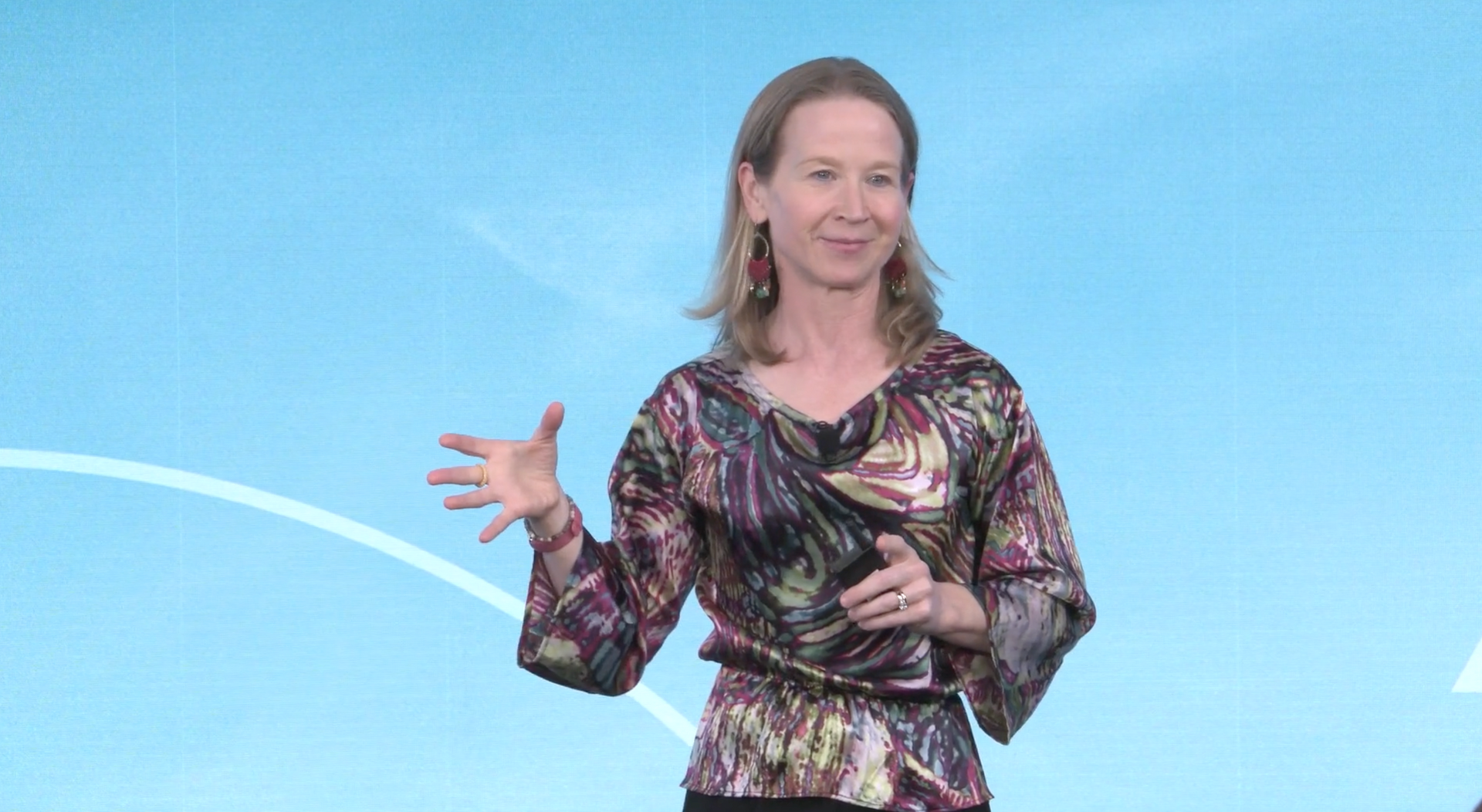 April Rinne in a floral shirt is standing in front of a blue background.