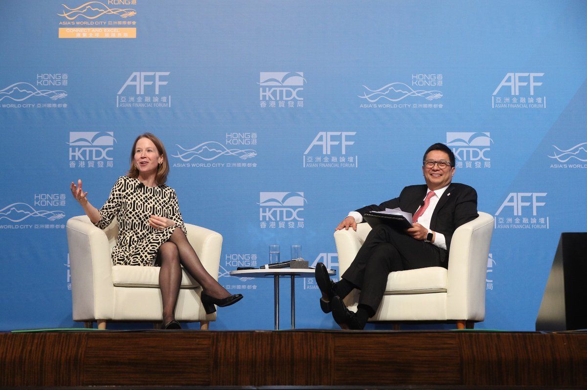 A man and April Rinne are sitting in chairs on a stage.