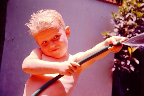 A shirtless young Jerry Michalski is holding a hose and spraying water